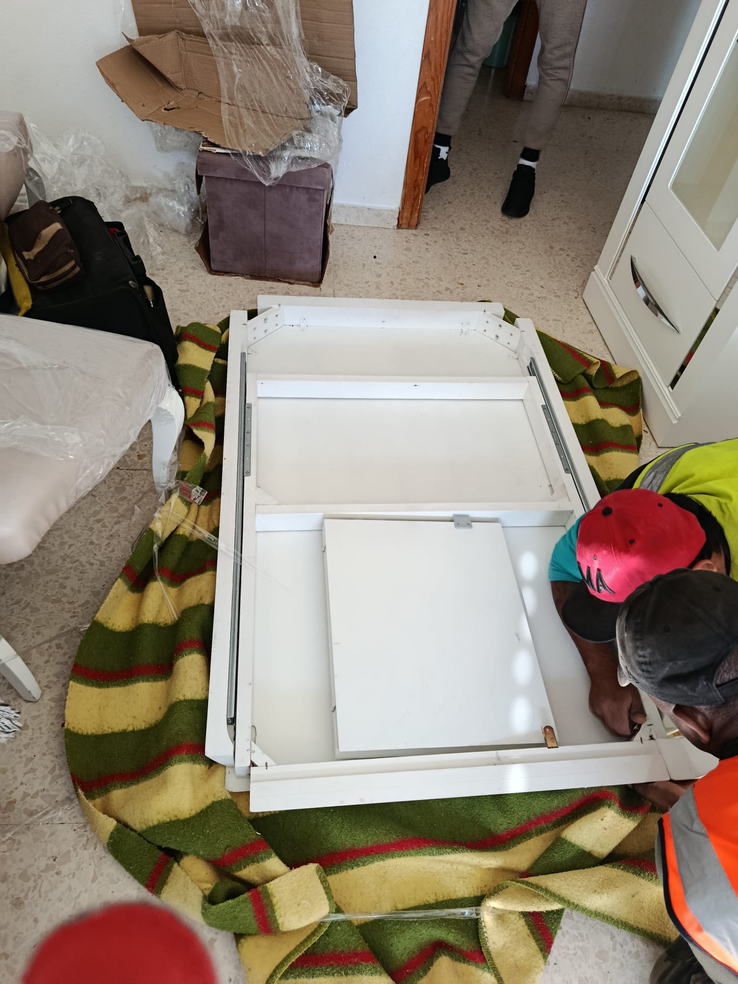 Operarios desmontando una mesa blanca sobre una manta protectora