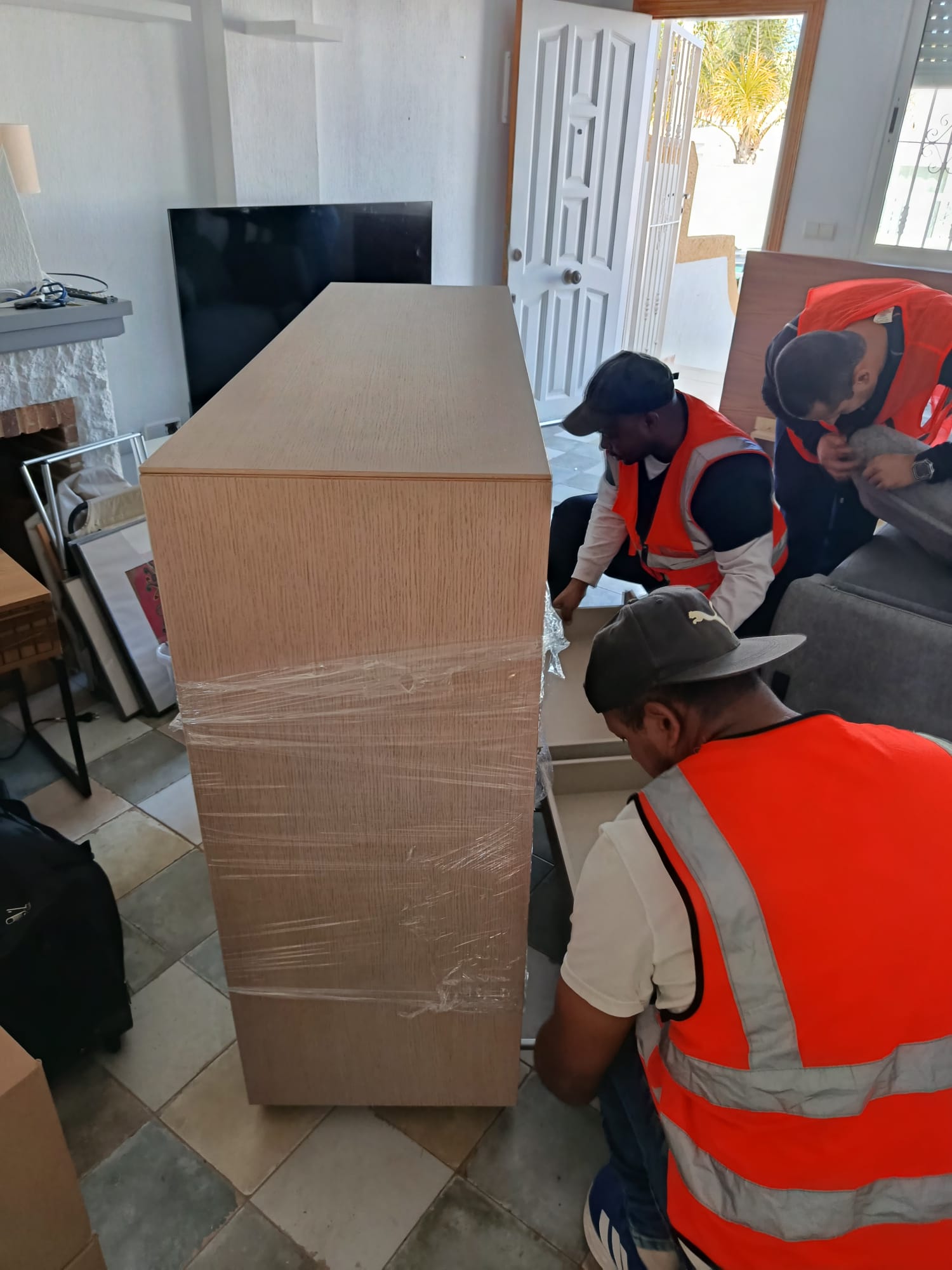 Operarios envolviendo un aparador de madera con film transparente