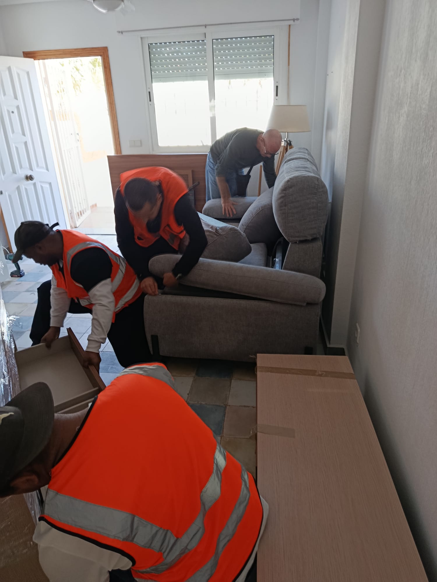 Tres trabajadores moviendo un sofá gris dentro de una vivienda